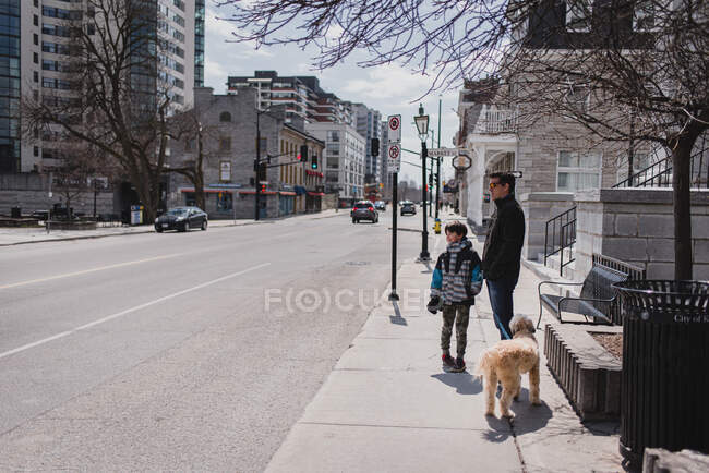 Vater und Sohn mit Hund stehen auf dem Bürgersteig einer ruhigen Stadtstraße. — Stockfoto