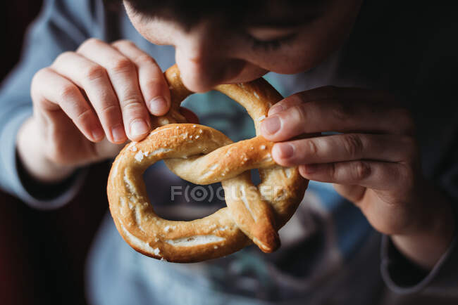 Gros plan d'un garçon qui mange un bretzel doux fait maison. — Photo de stock
