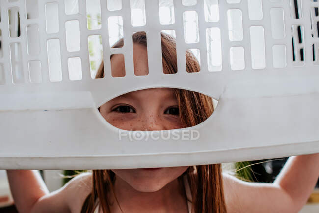 Goofy cute child peeking through laundry basket — Stock Photo