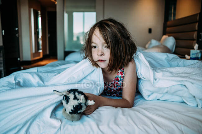 Menina com seu brinquedo deitado na cama no quarto — Fotografia de Stock