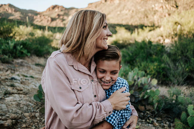 Madre che abbraccia sorridente bambino non binario nel deserto — Foto stock