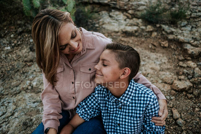 Mother hugging non binary child while sitting on rocks — Stock Photo