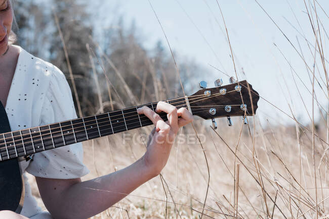 Vista della mano della donna che suona la chitarra in un campo in estate — Foto stock