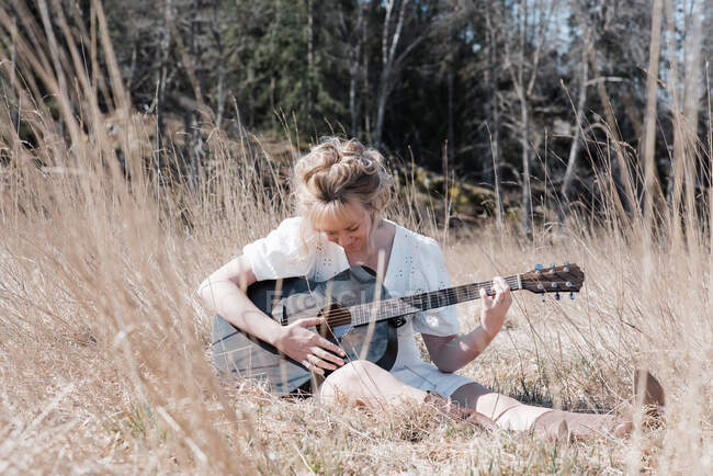 Woman sat in a field happily playing guitar in summer — Stock Photo