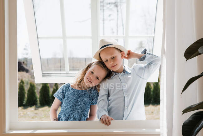Брат и сестра обнимаются, глядя в окно дома — стоковое фото