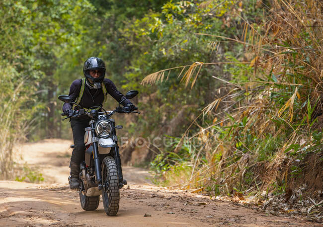 Woman riding her scrambler type motorcycle through forrest — Stock Photo