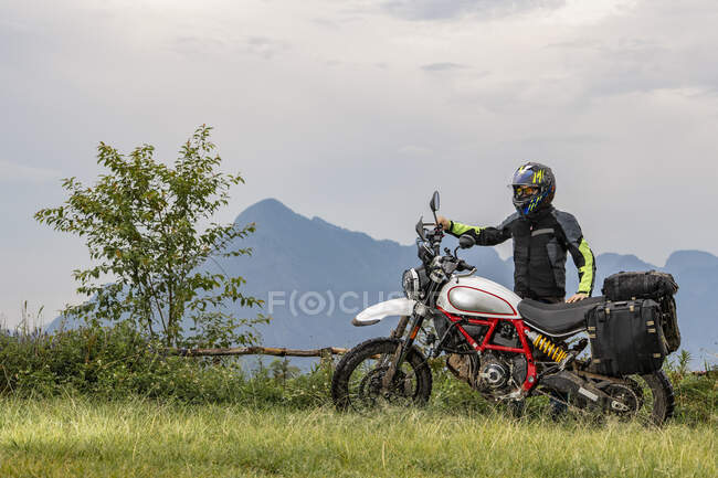 Человек, стоящий рядом со своим мотоциклом скремблер типа — стоковое фото