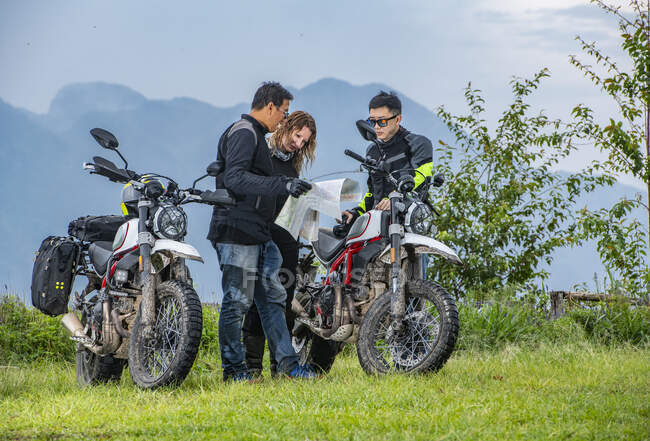 Tres amigos mirando el mapa en el viaje en motocicleta - foto de stock