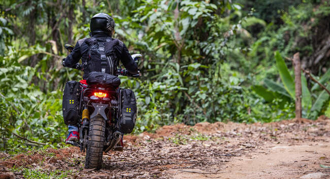 Femme chevauchant sa moto de type brouilleur à travers la forêt — Photo de stock