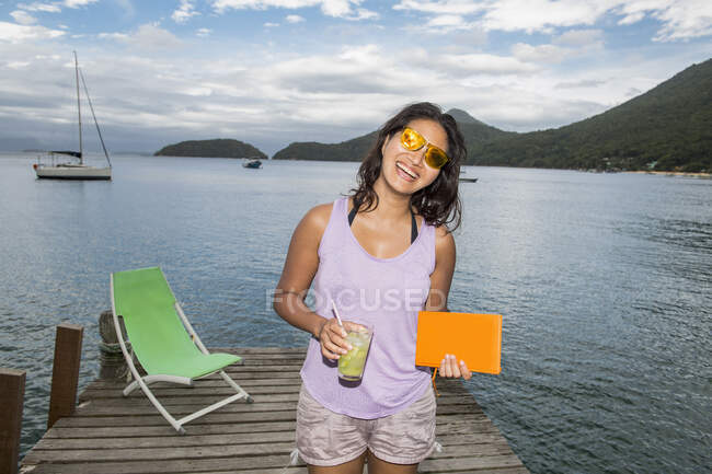 Mujer sosteniendo bebida en muelle en la isla tropical de Ilha Grande - foto de stock