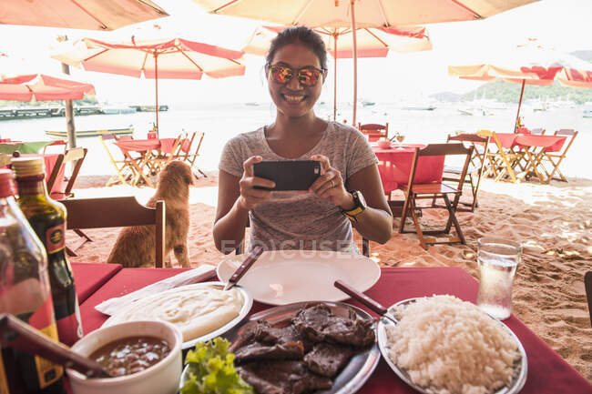 Woman at beach restaurant taking picture of food — Stock Photo