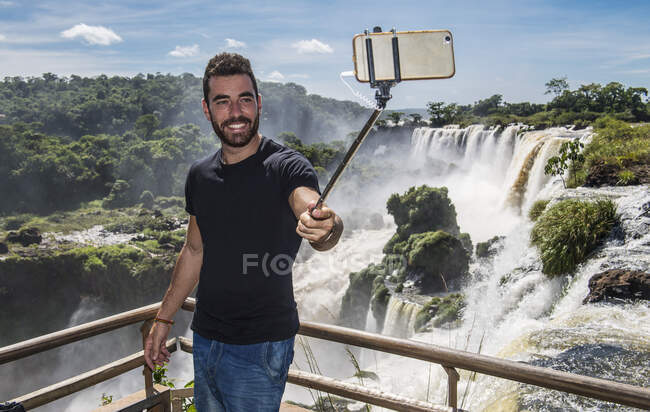 Hombre tomando una selfie con monópodo en cascadas de Iguazú en Argentina - foto de stock