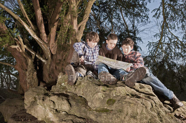 Tres chicos leyendo mapa en la cima de la roca - foto de stock
