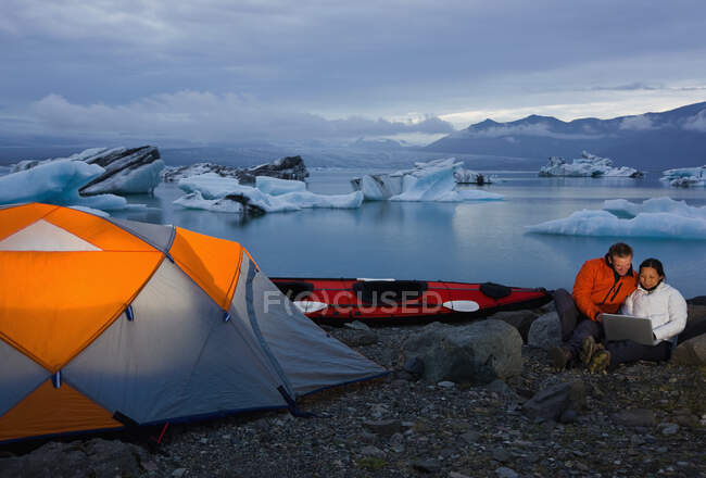 Couple regardant ordinateur portable sur le camping par lagon de glaciers en Islande — Photo de stock