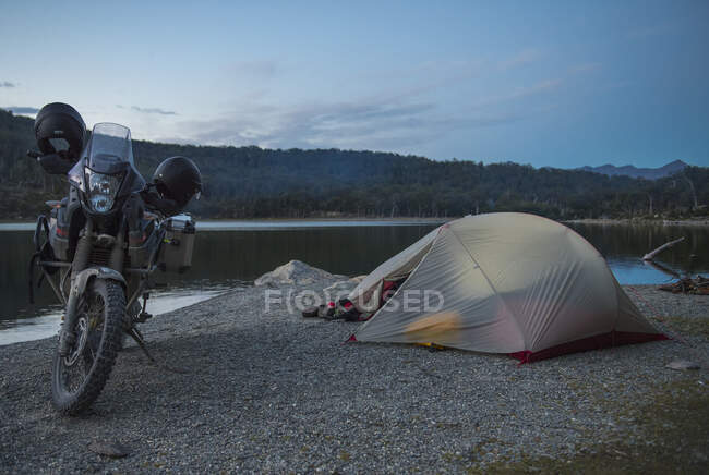 Acampamento com moto de turismo ao lado ainda lago na Tierra del Fuego — Fotografia de Stock