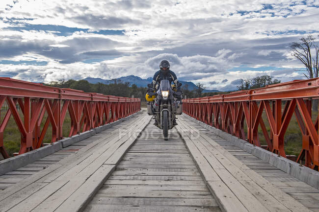 Чоловік на дорозі гастролює мотоциклом перетинаючи дерев'яний міст — стокове фото