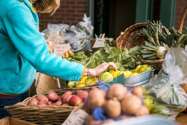 Mujer joven recogiendo verduras en el mercado de agricultores - foto de stock