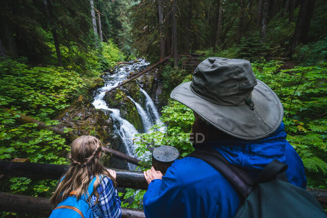 Man and daughter looking at waterfall from bridge — Stock Photo