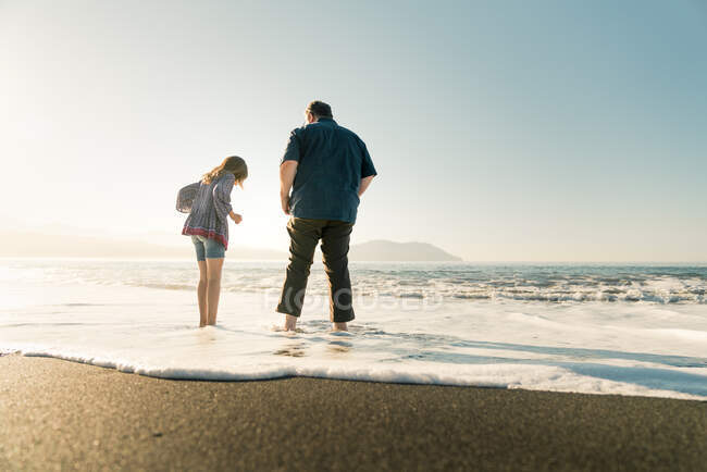 Батько і дочка стоять у воді на пляжі під час заходу сонця — стокове фото