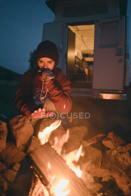 Mujer joven cogida de la mano cerca del fuego mientras acampa al atardecer - foto de stock