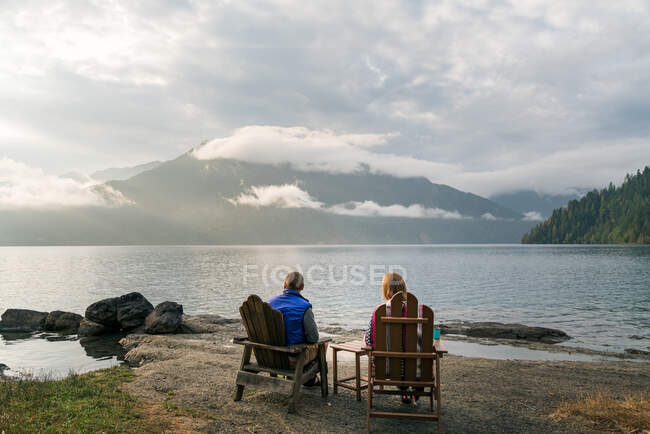Homme et femme assis au bord du lac pendant le coucher du soleil — Photo de stock