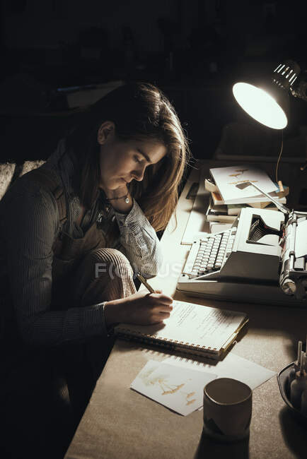 Mujer escribiendo por lámpara en el escritorio con máquina de escribir - foto de stock