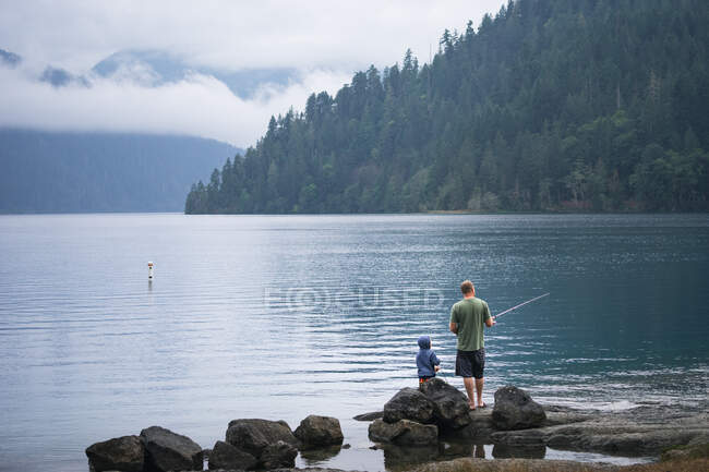 Отец и сын рыбачат на берегу живописного озера — стоковое фото