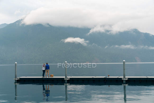 Man and woman standing on dock looking at foggy mountans — Stock Photo