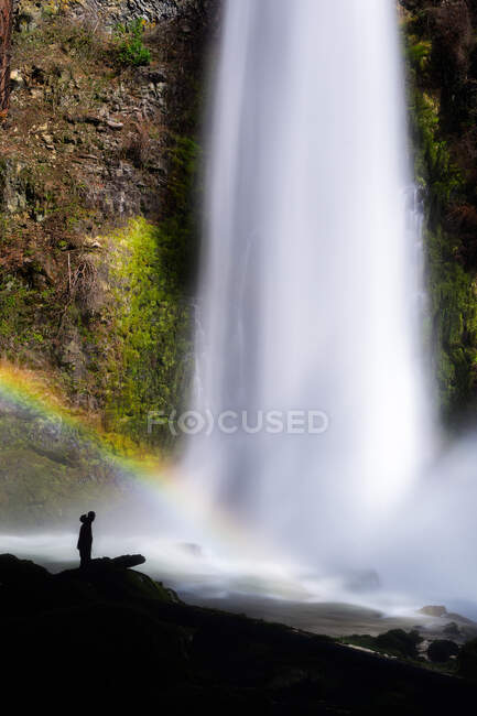 Silhueta de pessoa em uma cachoeira com um arco-íris — Fotografia de Stock