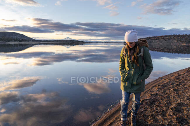 Молода жінка ходить уздовж озера на заході сонця з горою на задньому плані — стокове фото