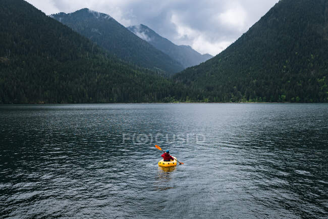 Людина в каяку веслує на озері до гір — стокове фото