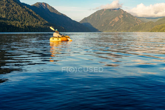 Jeune homme pagayant sur le lac vers la montagne au coucher du soleil — Photo de stock