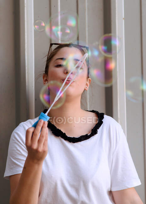 Молода жінка робить мильні бульбашки, спираючись на стіну — стокове фото