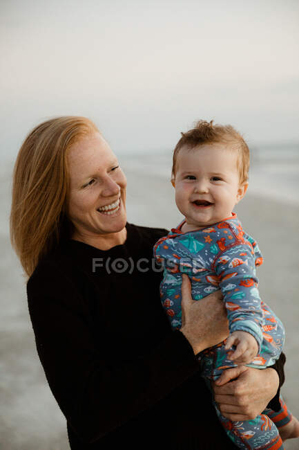 Young redhead mom laughs and holds laughing fat baby boy in onesie — Stock Photo