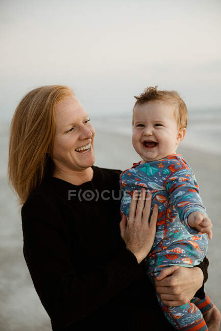 Single mom with red hair holds laughing chubby baby boy on the beach — Stock Photo