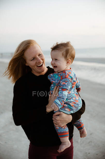 Молодая мама и здоровый пухлый мальчик ребенок улыбка во время прогулки на пляже — стоковое фото