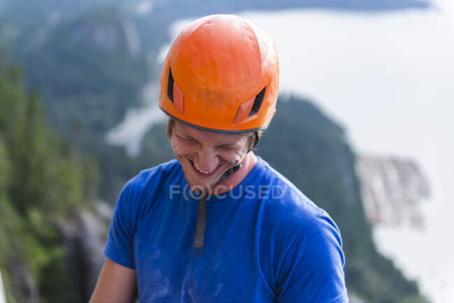 Bergsteiger mit Helm lächelt und lacht und blickt über Wasser — Stockfoto