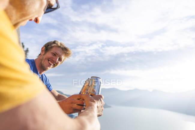 Двоє людей підбадьорюють, коли п'ють пиво на заході сонця. — стокове фото