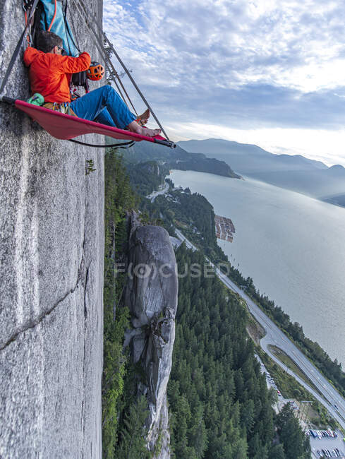 Side view of man sitting on portaledge organizing gear at sunset — Stock Photo