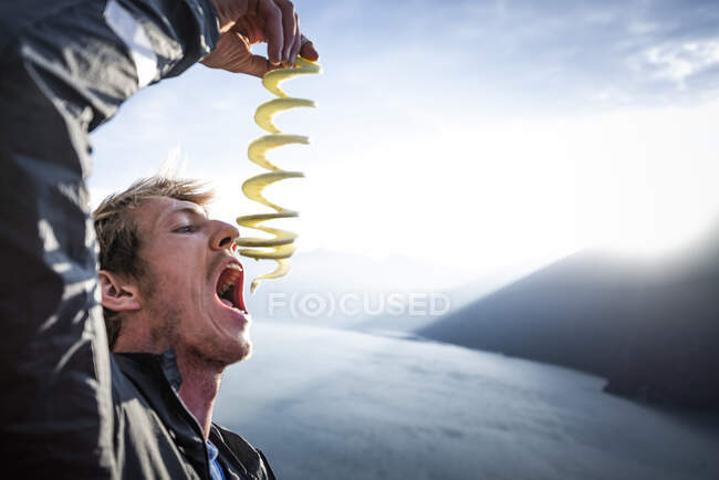 Людина їсть яблуко після того, як використовує яблучний пилок на заході сонця над морським сквамішем — стокове фото