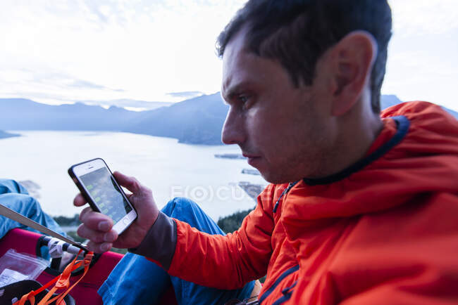Perplex man looking at phone sitting on portaledge at sunset thinking — Stock Photo