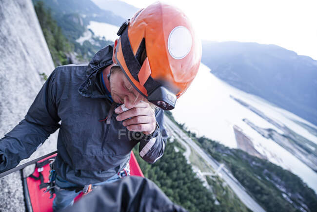 Climber with helmet scratching his nose standing on portaledge sunset — Stock Photo