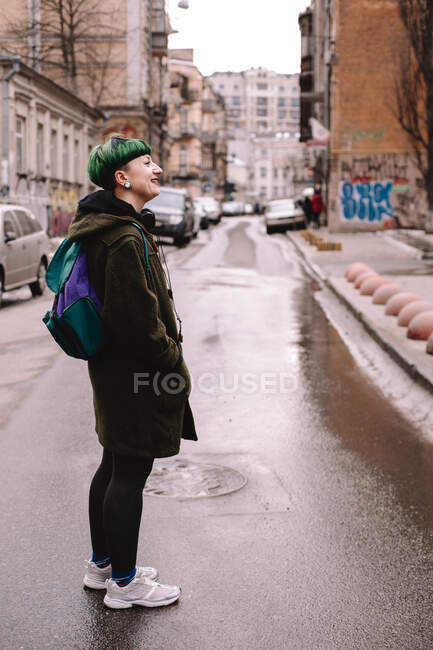 Joyeux hipster féminin non binaire debout sur la route en ville — Photo de stock