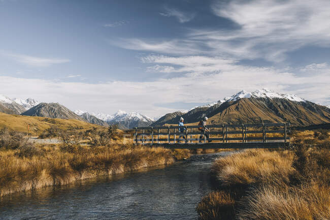 Pareja de jóvenes excursionistas cruzando un arroyo en el lago Clearwater, Alpes del Sur, Nueva Zelanda. - foto de stock