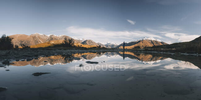 Panorama of a young woman standing in front of a puddle, Canterbury, New Zealand. — Stock Photo