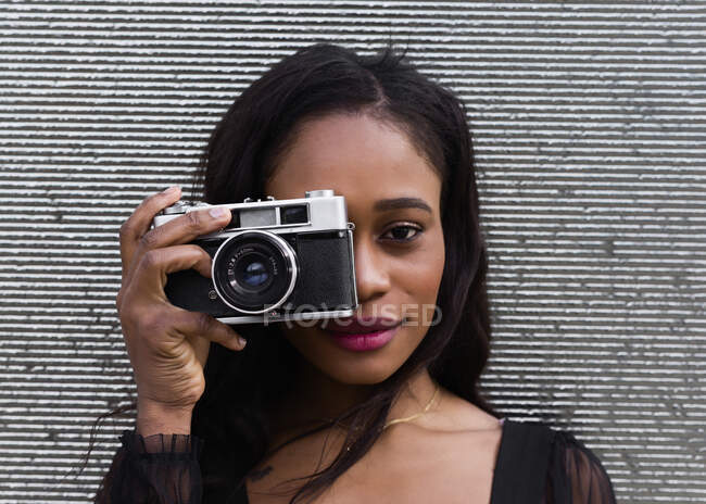 Retrato de una joven afroamericana posando con una cámara - foto de stock