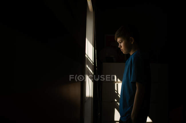 Jeune adolescent garçon regardant par la fenêtre pendant l'isolement — Photo de stock
