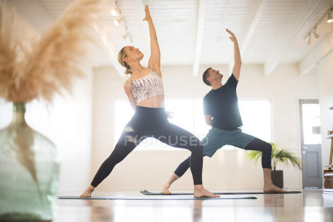 Um casal em reverso guerreiro pose durante ioga. — Fotografia de Stock