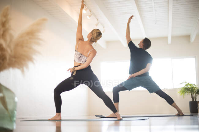 Un couple en posture guerrière inversée pendant le yoga. — Photo de stock