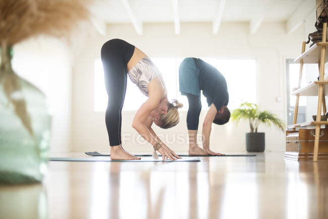 Una coppia in posizione piega in avanti durante lo yoga. — Foto stock